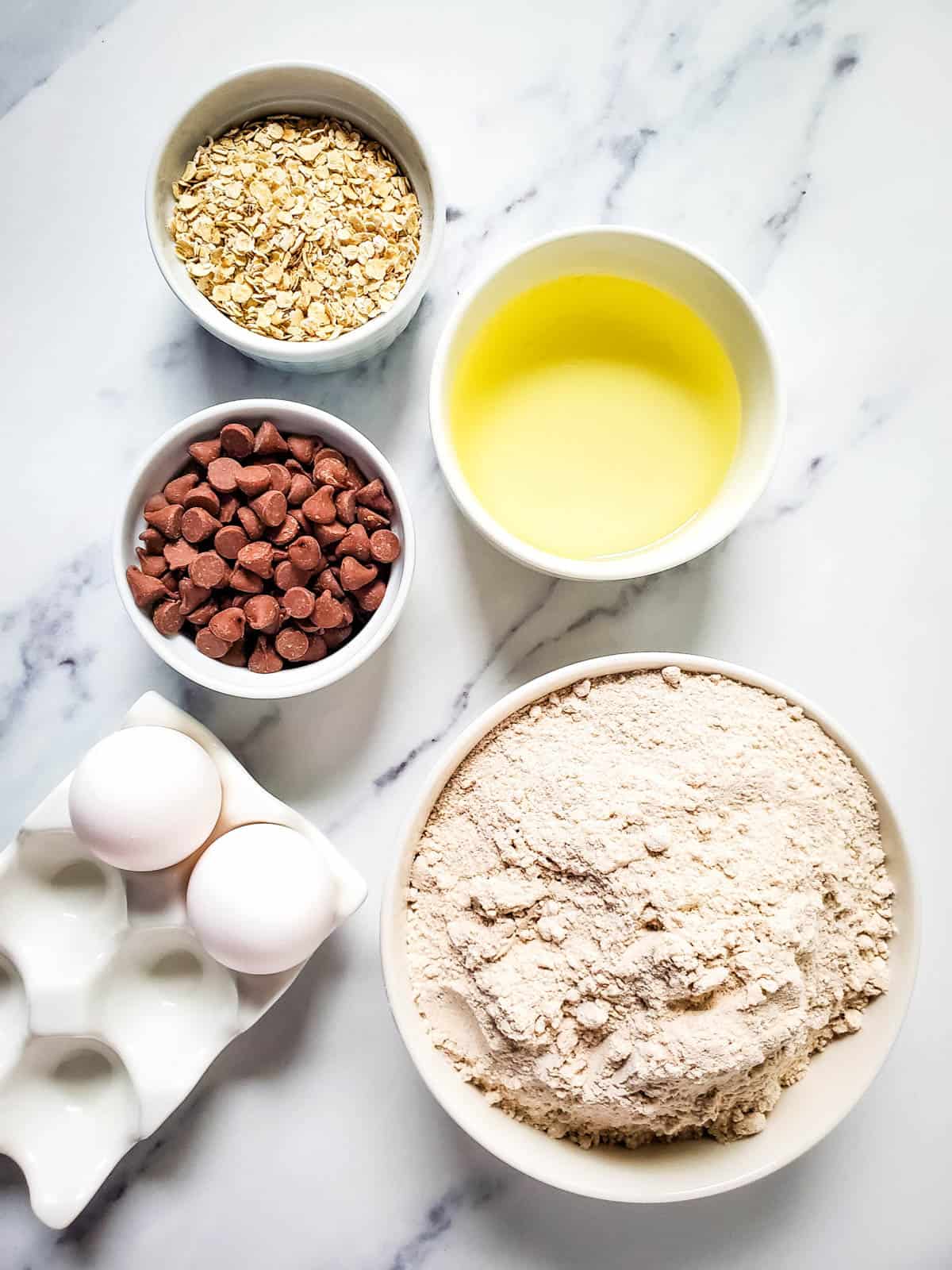The ingredients to make Oatmeal Cake Mix Cookies with chocolate chips in small bowls on a table.