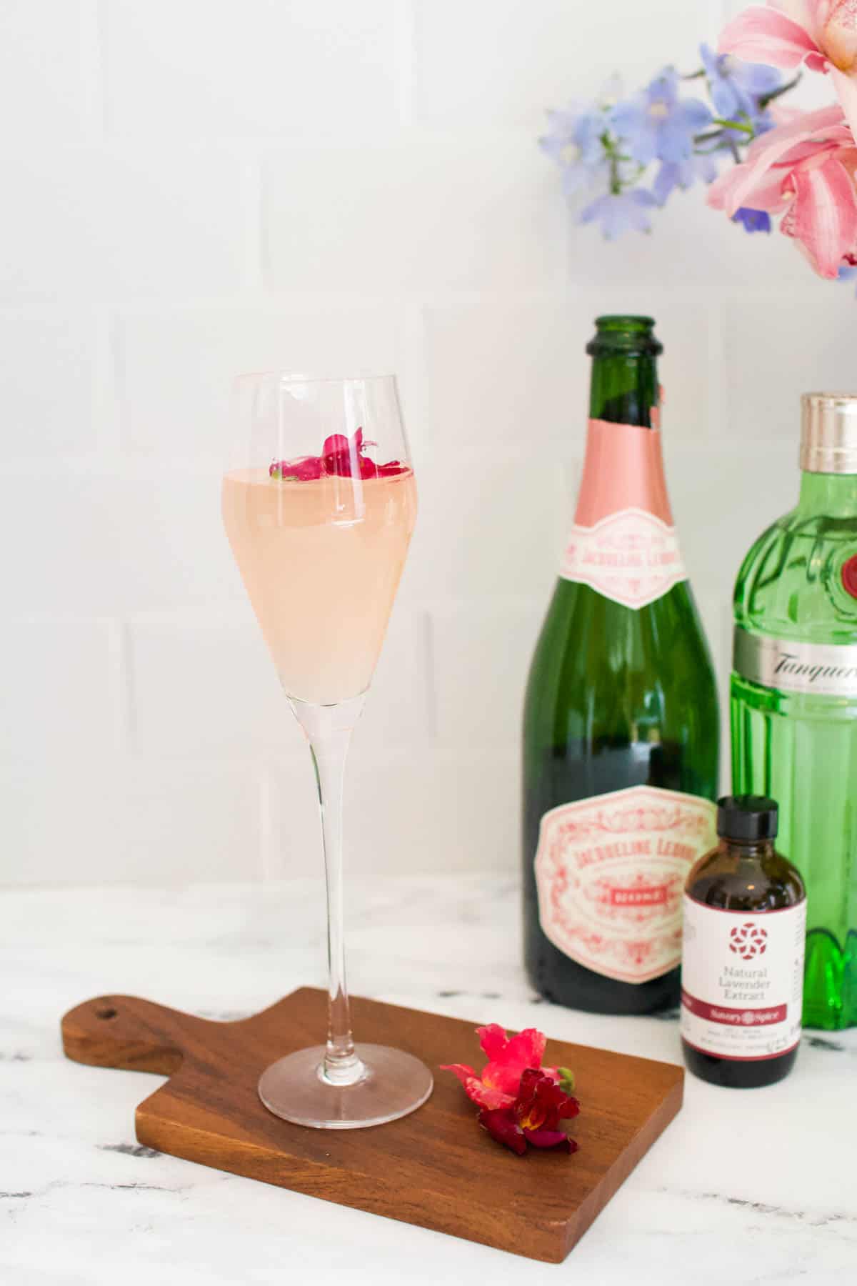 Lavender French 75 in a champagne flute next to the bottles that went into making the drink. 