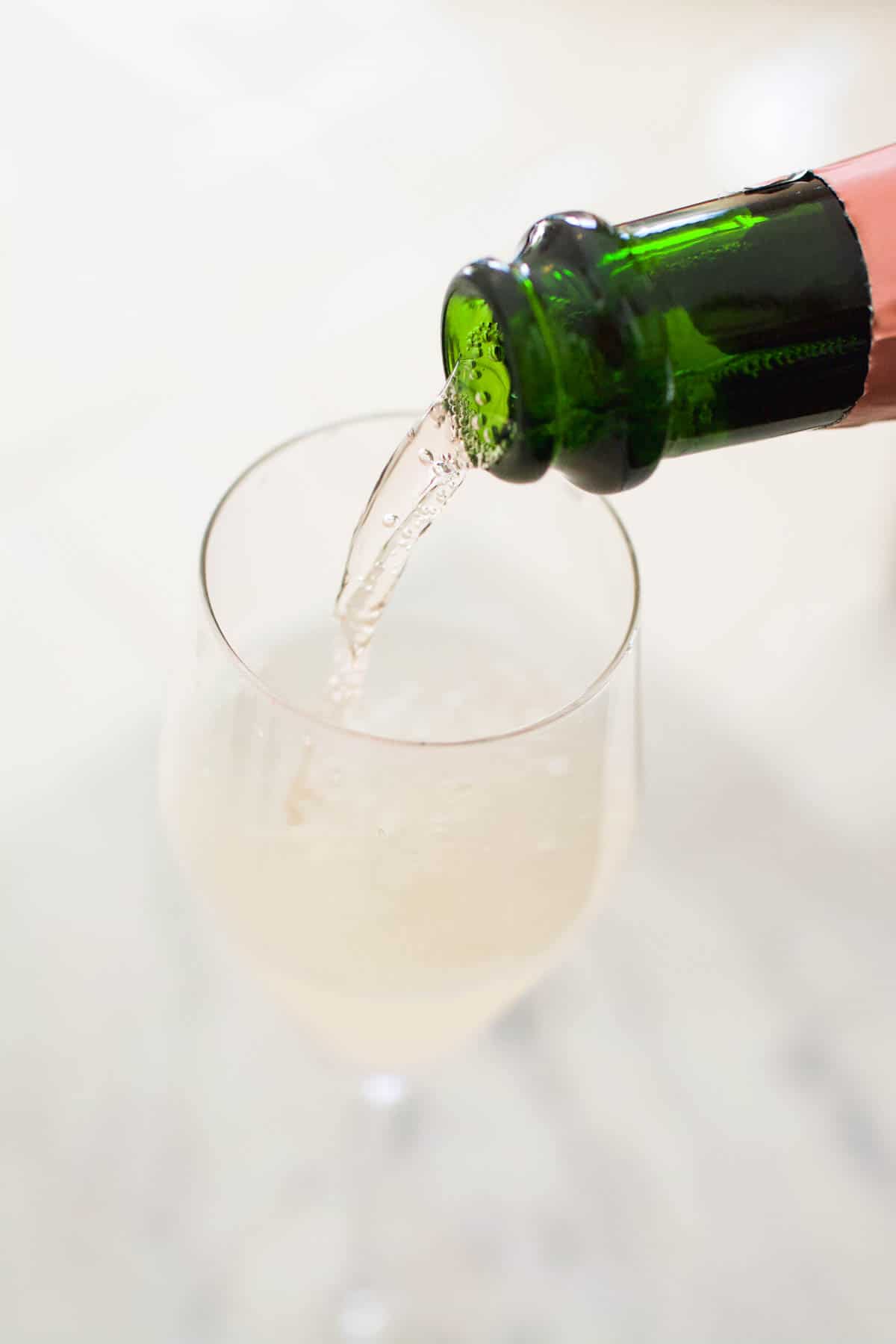 Cocktail in a champagne flute being topped up with pink champagne. 