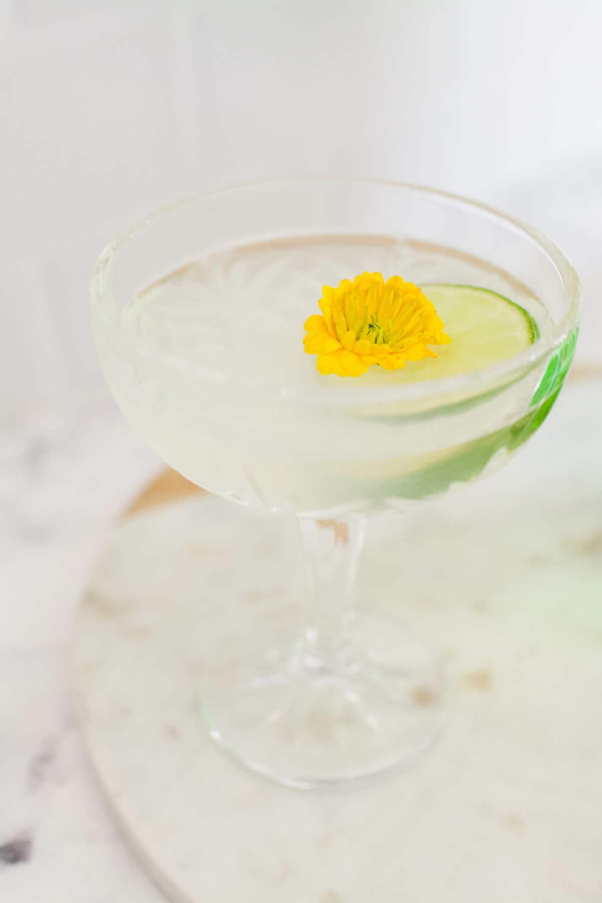 Gin gimlet in a coupe glass garnished with a lime wheel and a yellow edible flower.