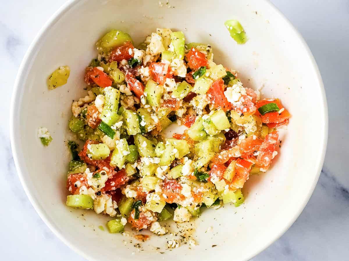 A bowl of chopped tomatoes and cucumbers tossed in a Mediterranean dressing.