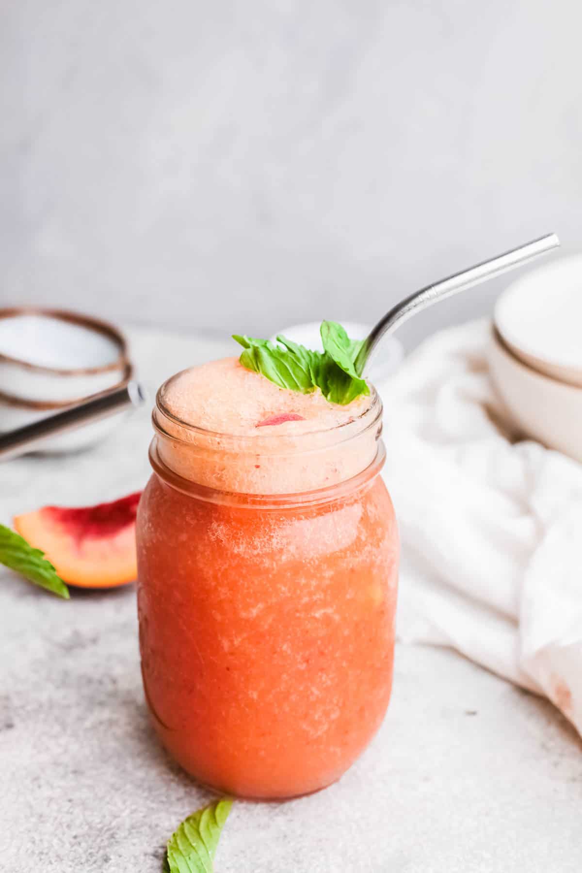 Peach Froze served in a jar garnished with fresh mint and a metal straw.