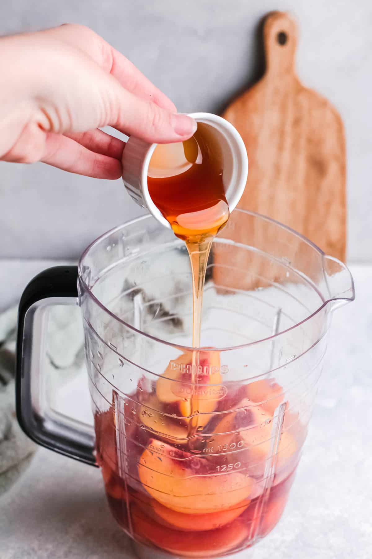 Runny honey being poured into a blender with sliced peaches and rose wine.