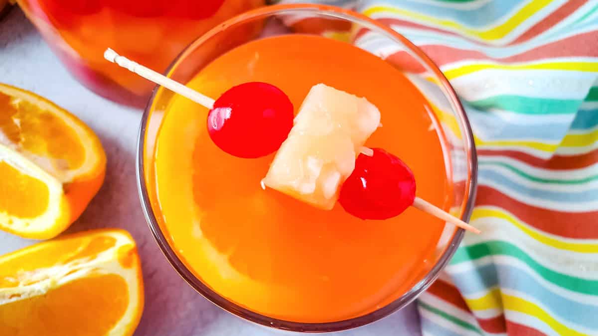 An overhead shot of a glass of passion fruit sangria with a toothpick garnish of cherries and pineapple chunk.