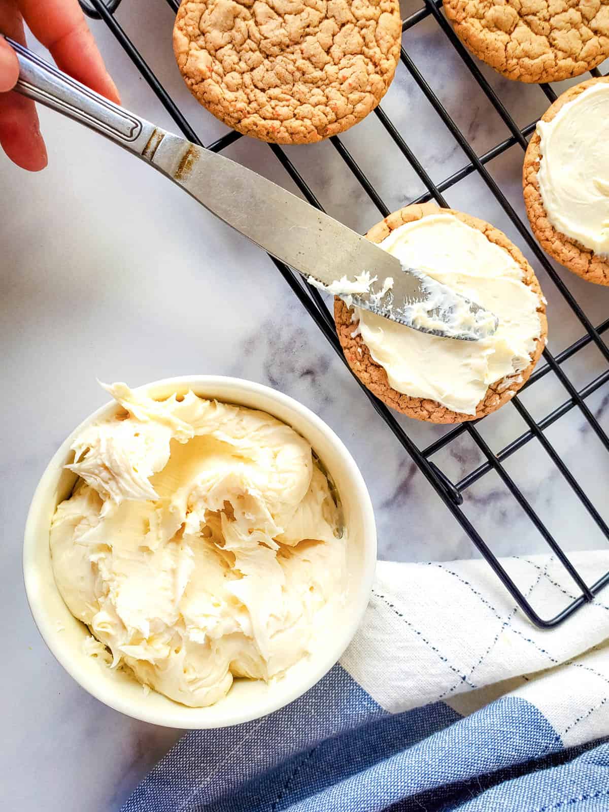 Someone using a knife to frost carrot cake mix cookies with cream cheese frosting.