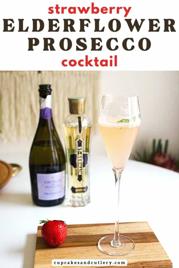 Strawberry Elderflower Prosecco cocktail in a champagne flute on a wooden tray next to a strawberry, St Germain bottle and bottle of Prosecco.