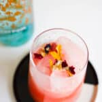 Watermelon juice and gin on the rocks garnished with edible flowers.