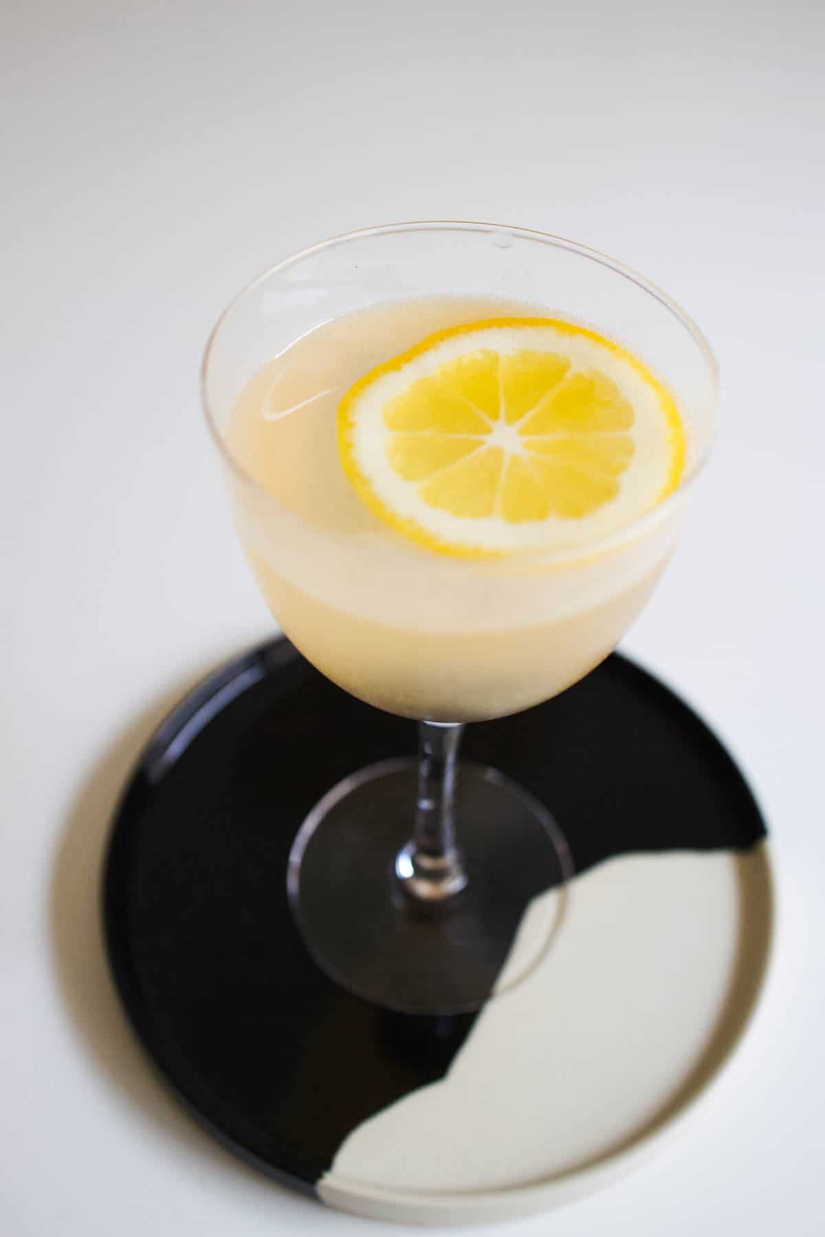 Cocktail on a black and white tray garnished with a lemon wheel.