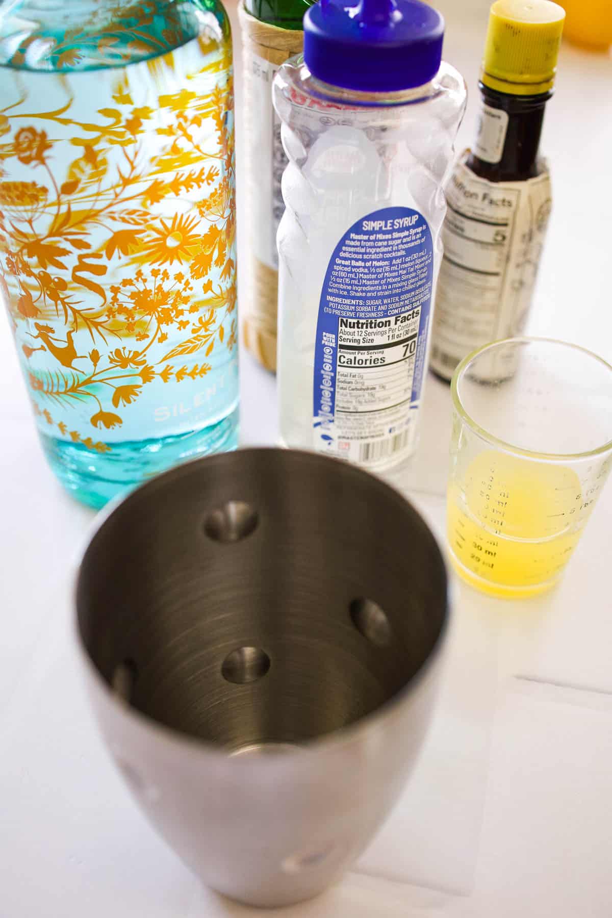 Cocktail shaker next to cocktail ingredients.