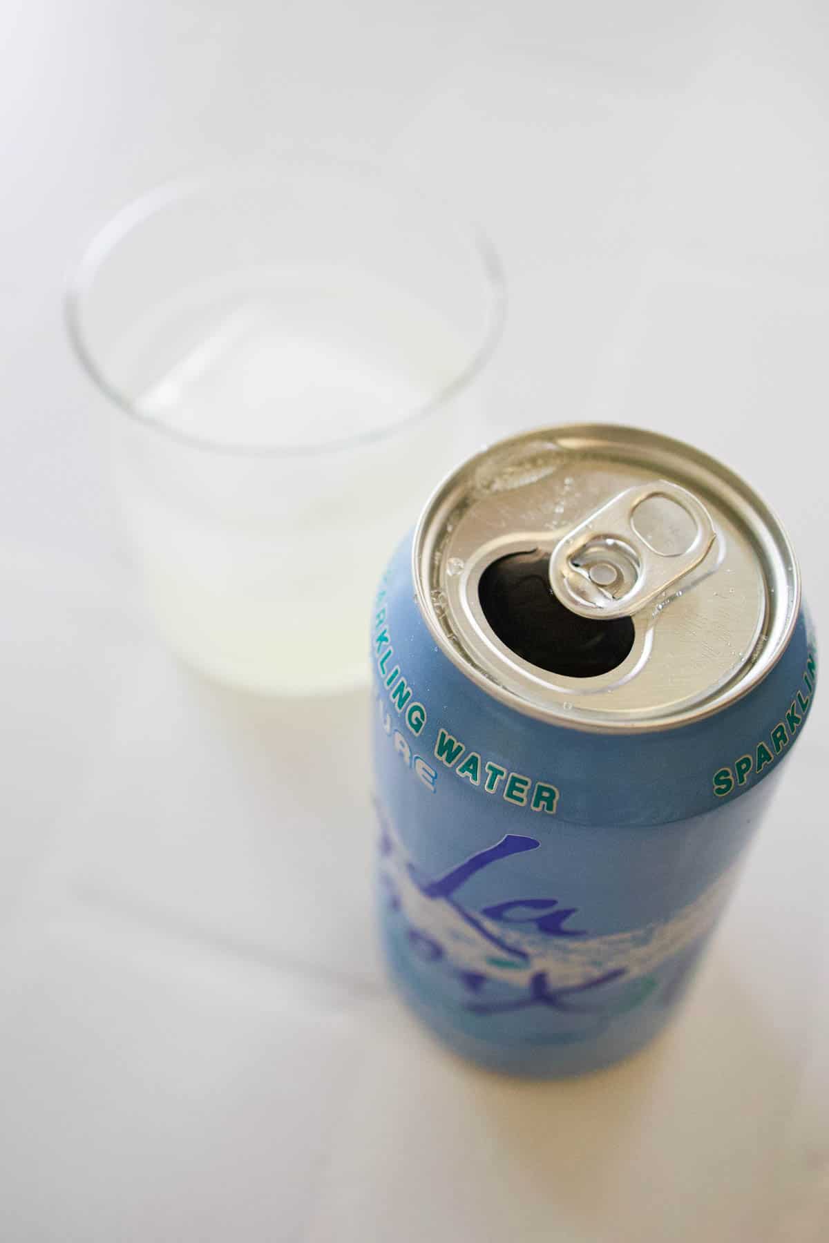Open can of LaCroix next to a cocktail in a glass.