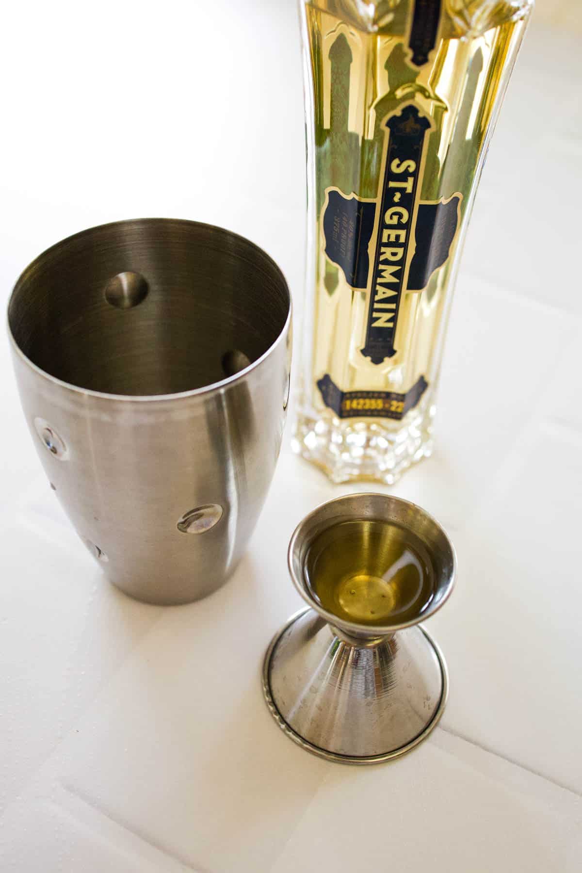 Cocktail shaker and jigger next to a bottle of St Germain.