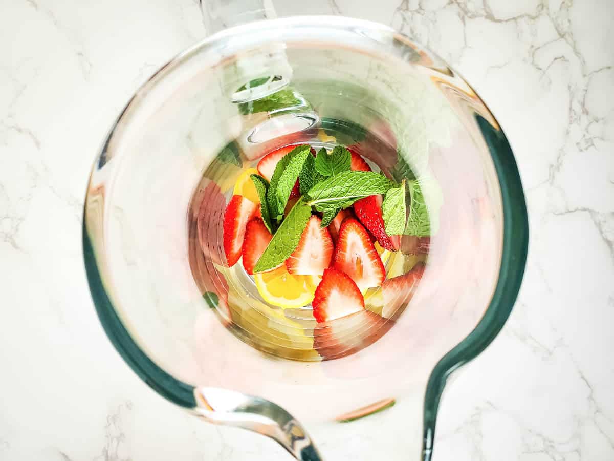 Close up of strawberries, lemon slices and fresh mint at the bottle of a glass pitcher.