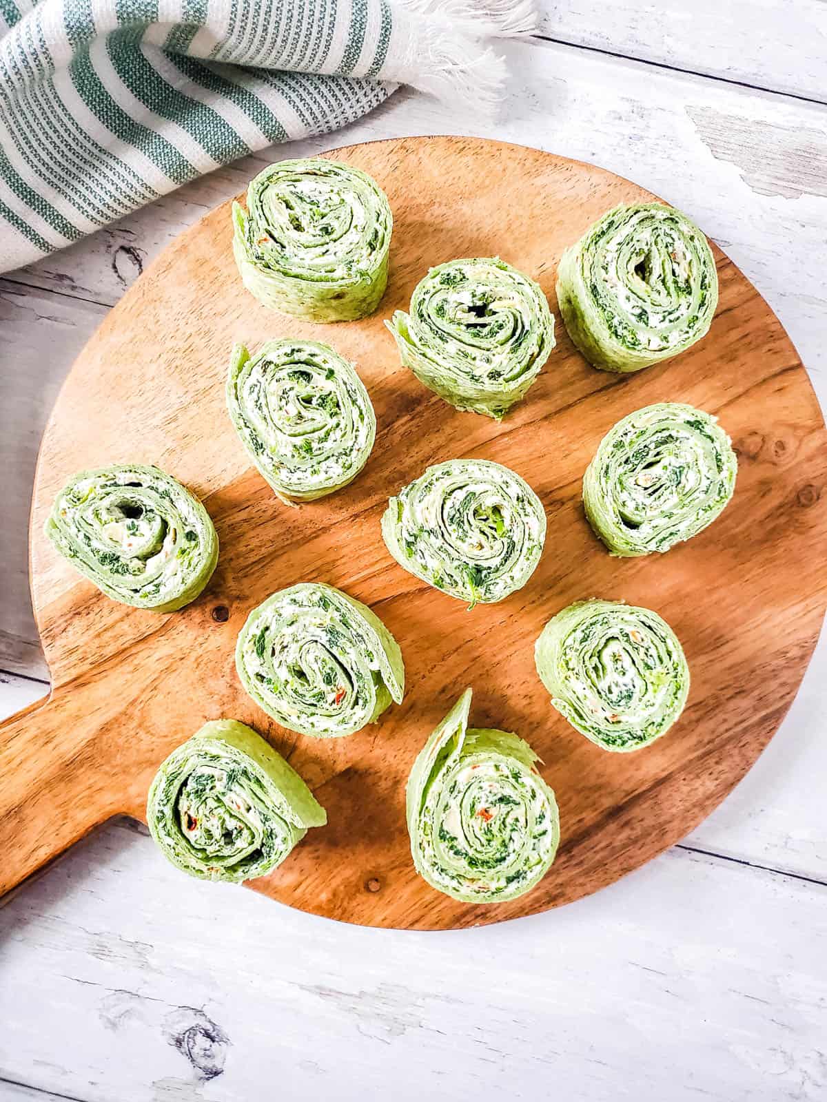A wood platter containing spinach pinwheels.