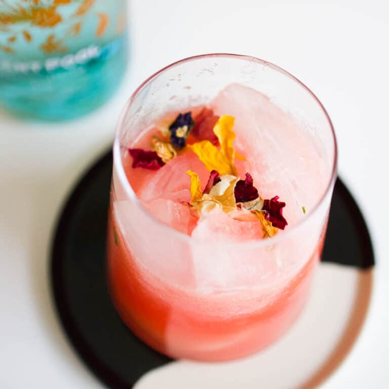 Close up of a watermelon cocktail on the rocks garnished with edible dried flowers.