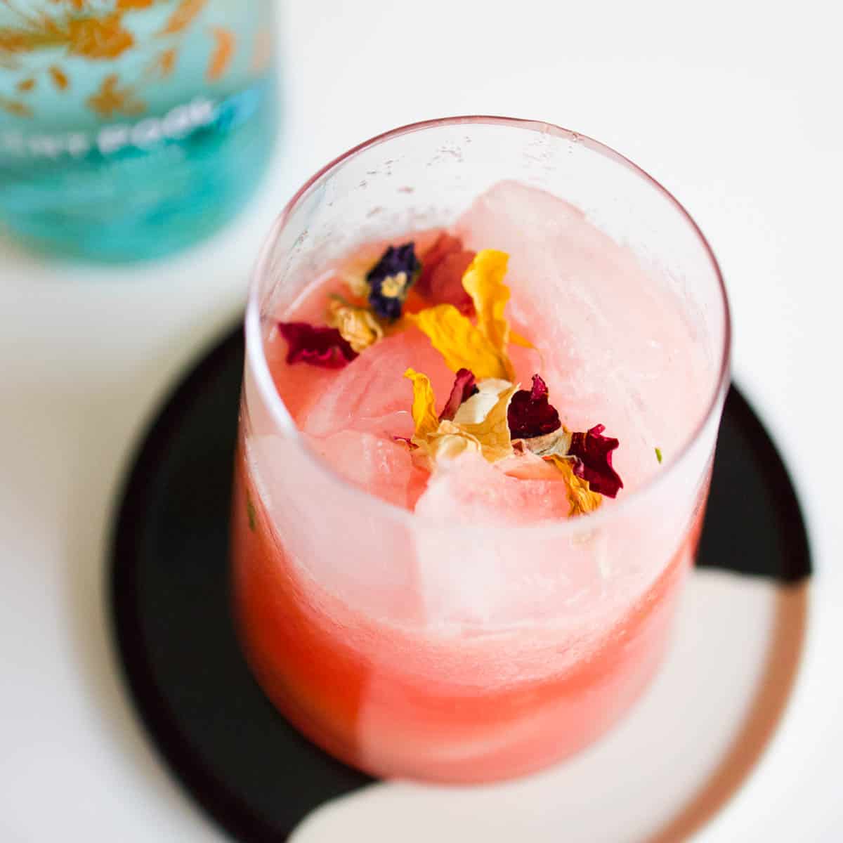 Close up of a watermelon cocktail on the rocks garnished with edible dried flowers.