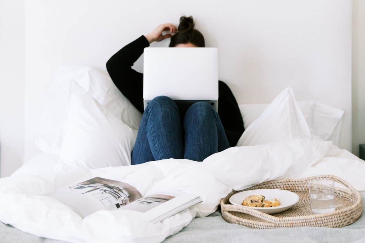 Woman sitting in a bed with a laptop and a tray with breakfast.