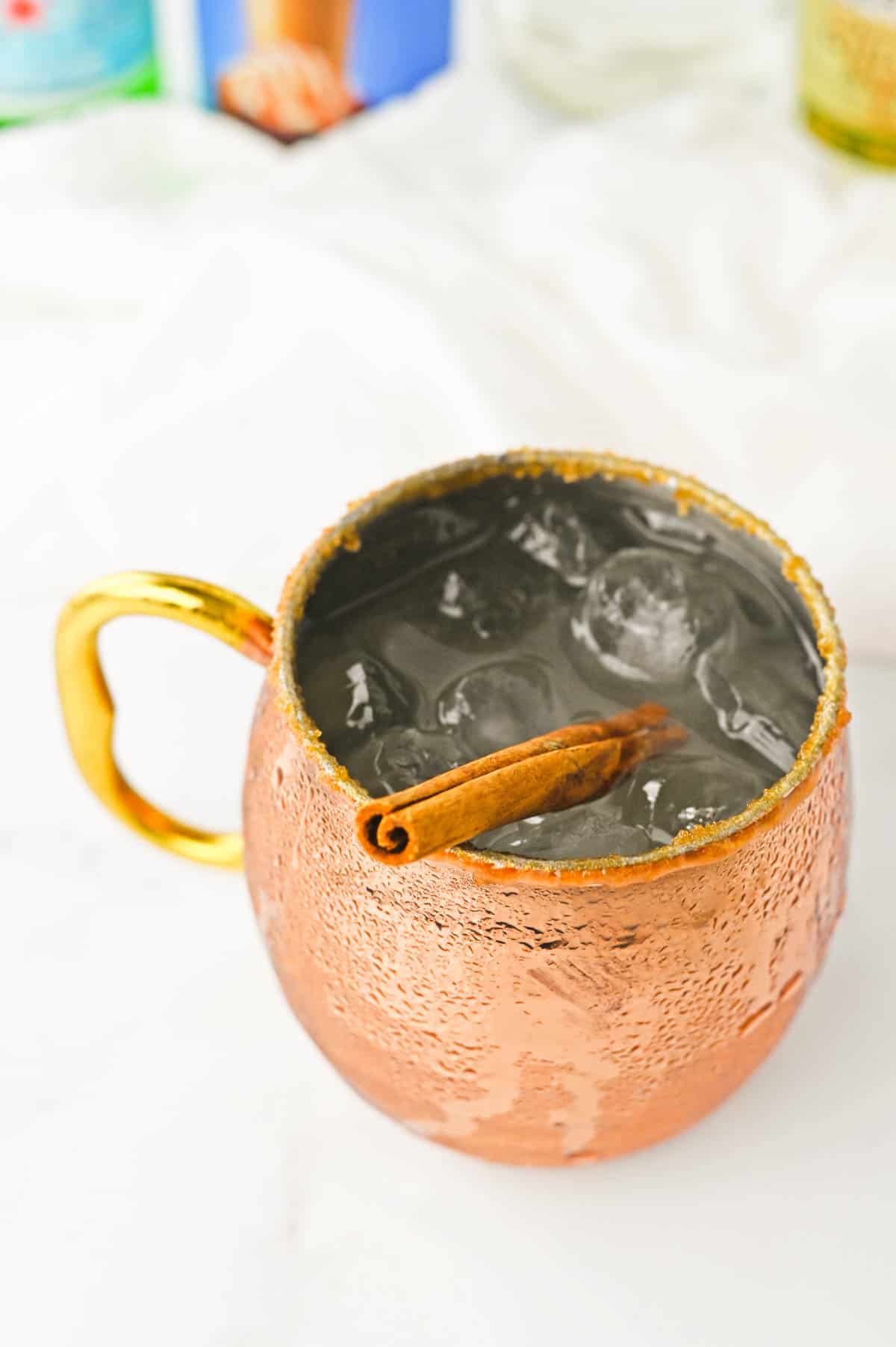 Moscow Mule in a copper mug with a salted caramel rim garnished with a cinnamon stick.