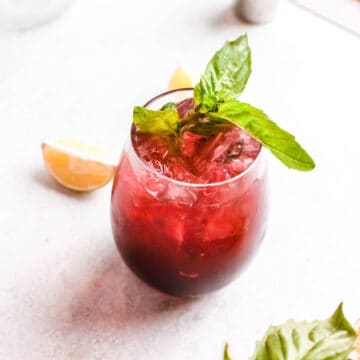 Cherry cocktail in a glass of ice garnished with a fresh basil sprig.