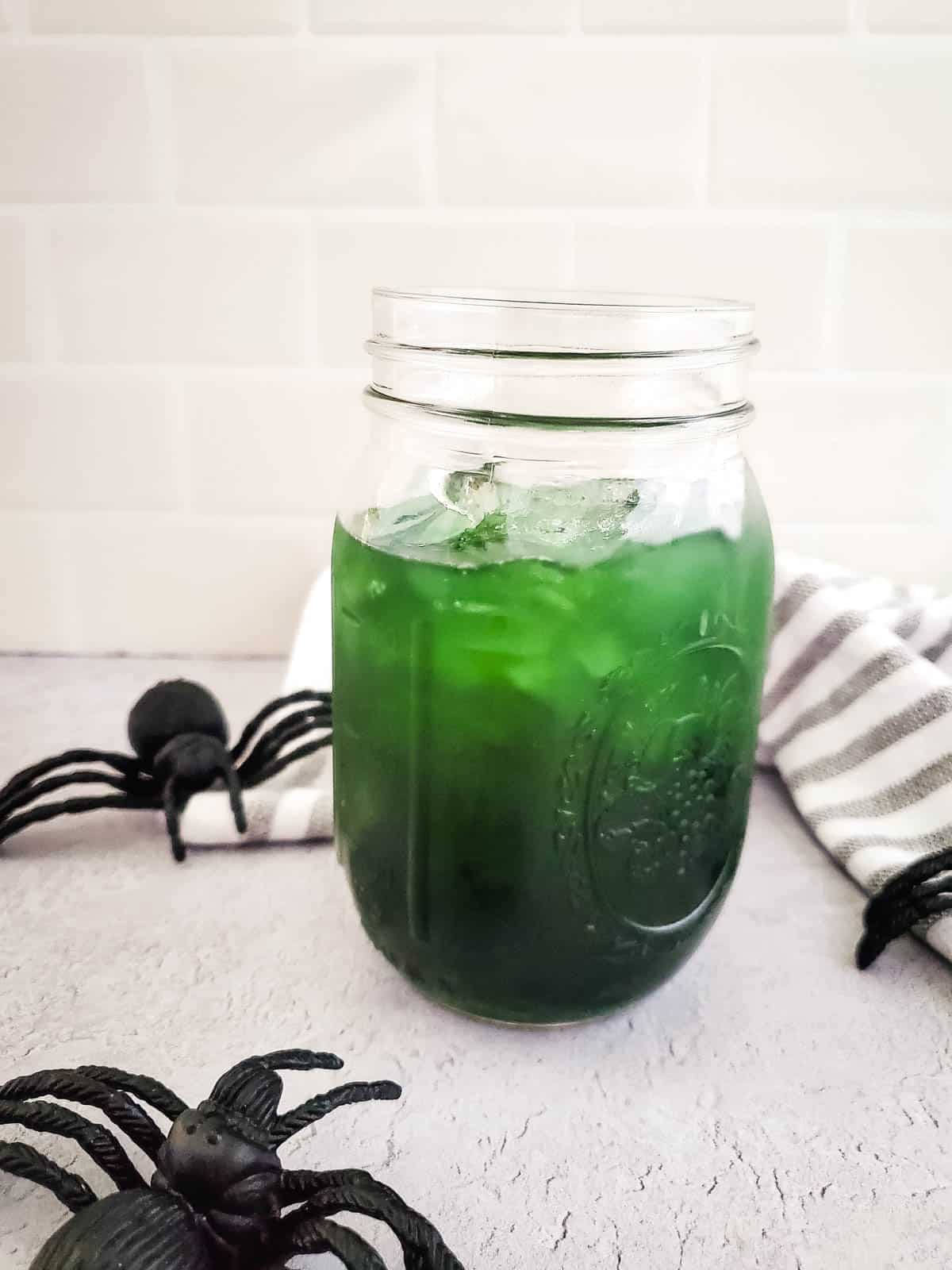 Halloween Margarita in a mason jar surround by black plastic spiders.