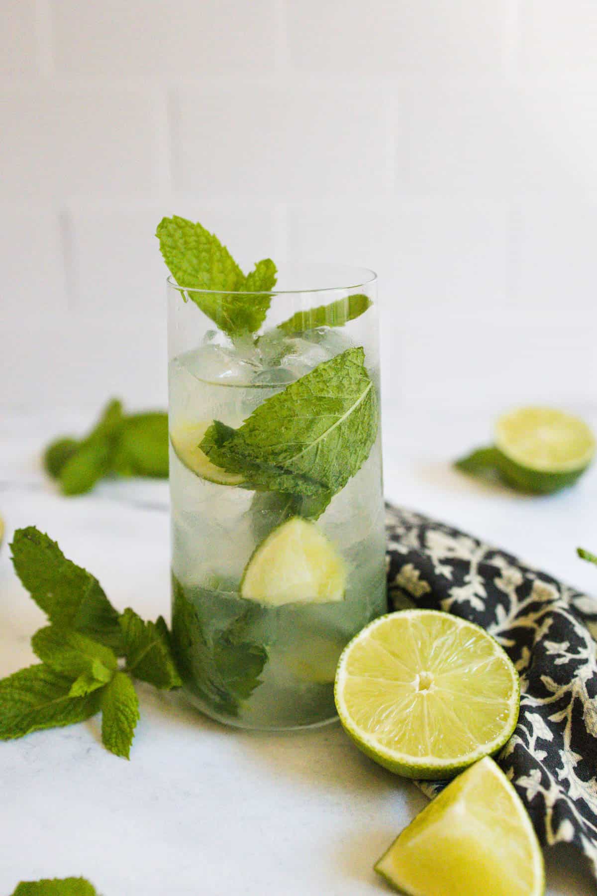Mojito on a white countertop with limes and mint sprigs.