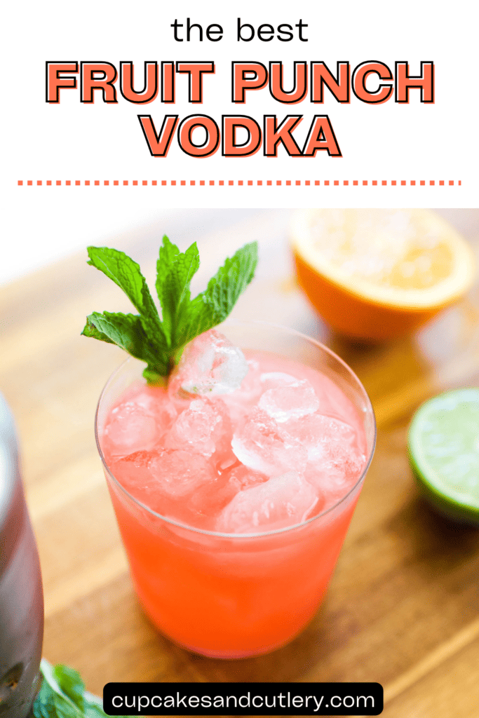 Text: The best fruit punch vodka with a pink cocktail on a cutting board garnished with a mint sprig next to a cut lime and orange.