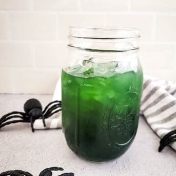 Green Halloween cocktail in a mason jar surrounded by plastic spiders.