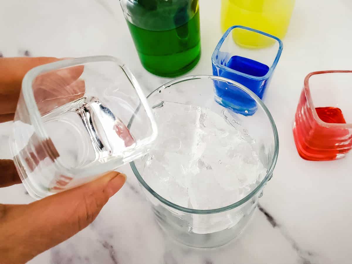 Tequila being poured over ice in a glass.