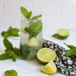 Mojito on a white countertop with cut limes and sprigs of fresh mint.