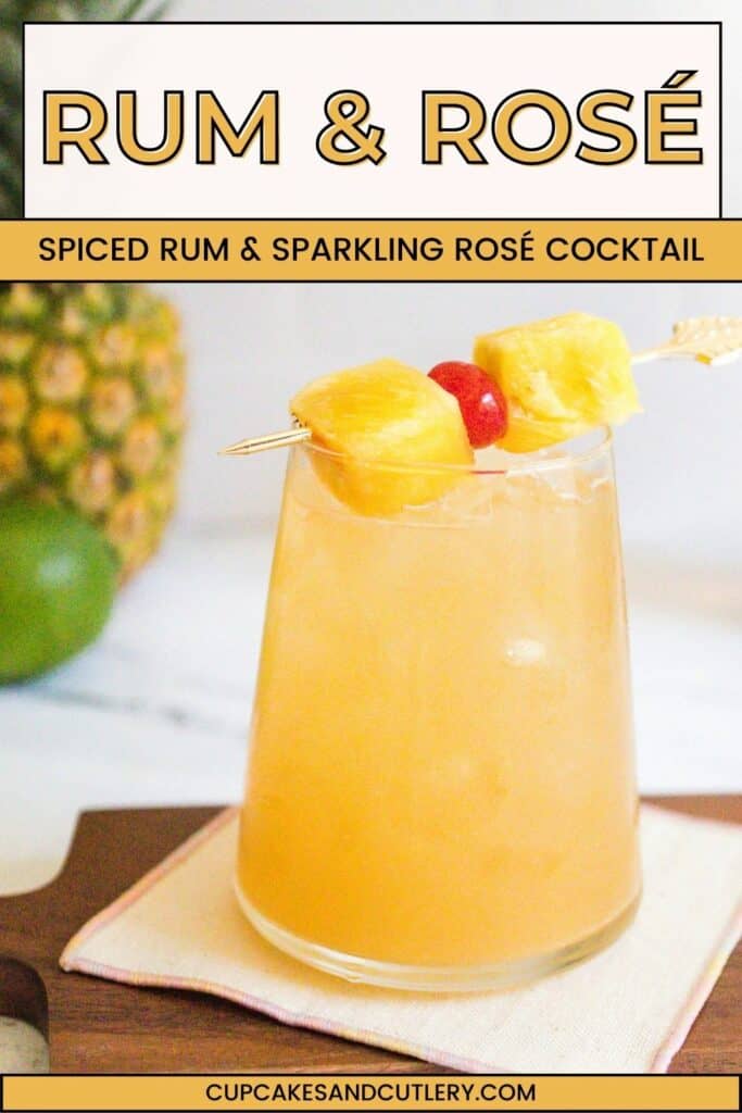 Close up of a rum and rose wine cocktail garnished with pineapple chunks and a cocktail cherry on a cocktail stick.