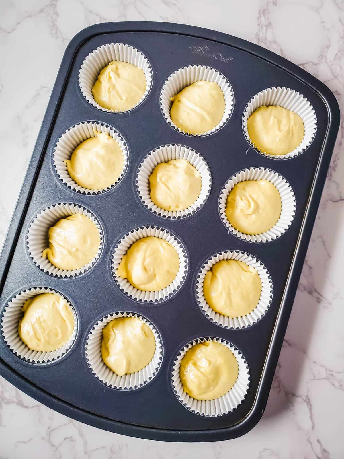 Spiced rum cupcake batter in cupcake liners in a tin on a counter.