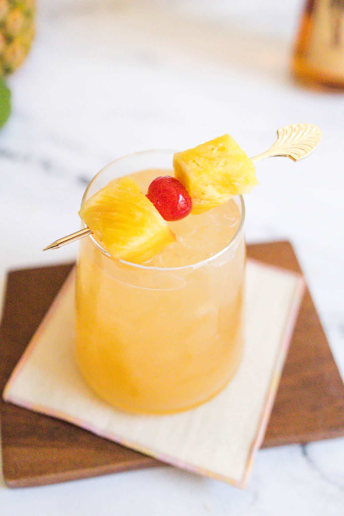 Tropical fruit cocktail garnished with pineapple chunks and a cocktail cherry on a cocktail stick.