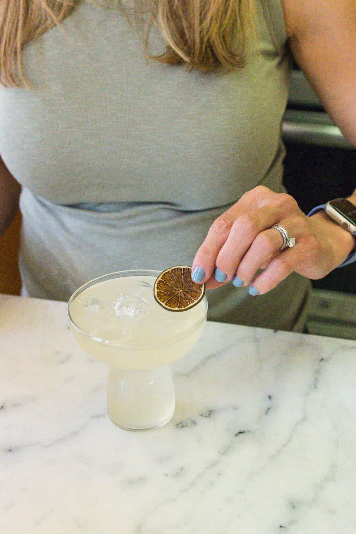 Woman garnishing a margarita with a dried lime wheel.