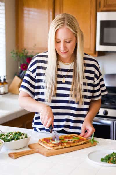 Woman cutting a pizza on a kitchen counter.