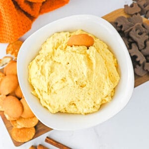 A white bowl holding a pumpkin fluff dessert with cookies around it and an orange towel.