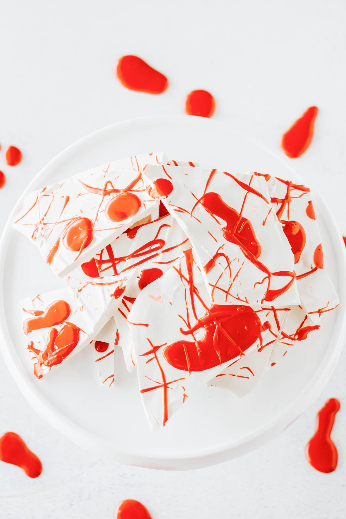 A white plate stacked with white chocolate bark pieces decorated with red icing to look like blood for Halloween.
