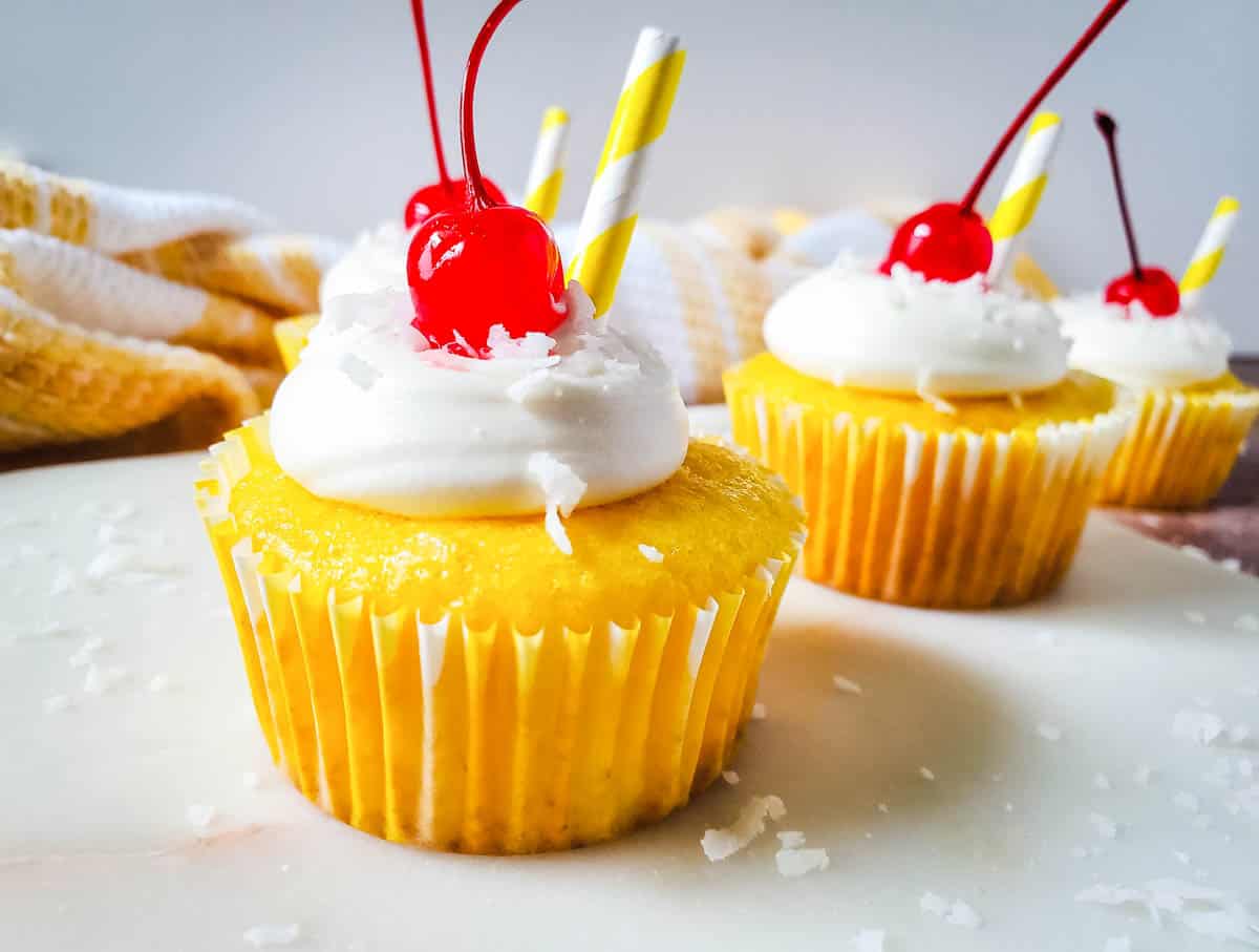 Rum infused pina colada cupcakes with shredded coconut vanilla frosting topped with maraschino cherries.