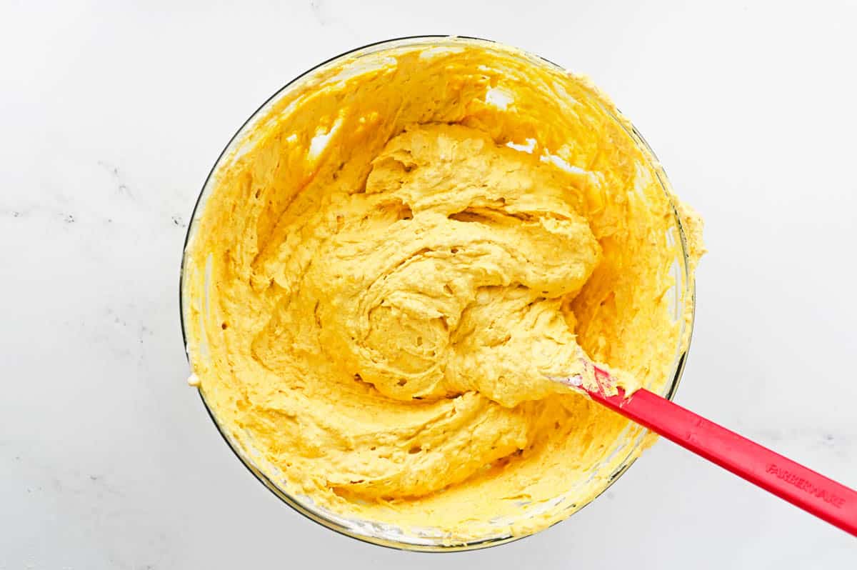 A mixing bowl with pumpkin and cool whip for a dessert dip mixed together with a spatula.