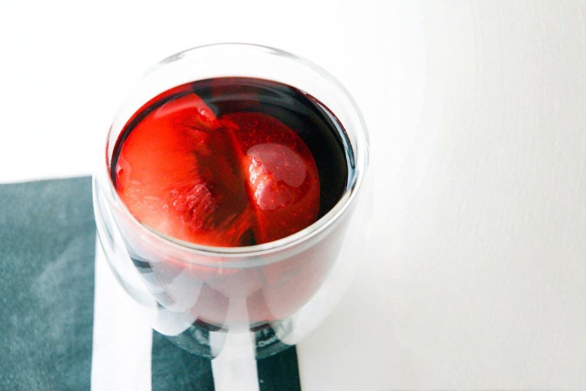 Warm fall sangria in an insulated glass handleless mug with plums.