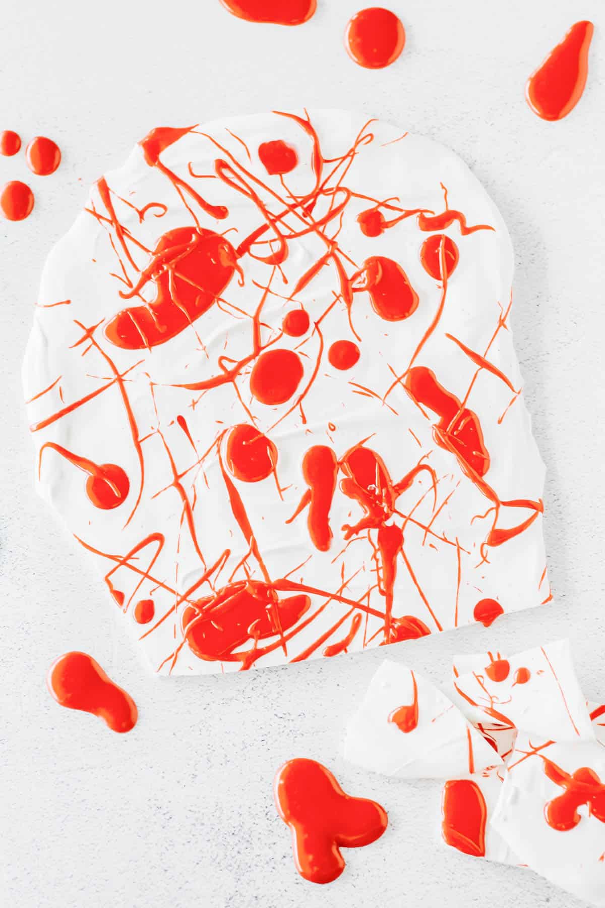 Hardened white chocolate bark on wax paper drizzled with red icing to look like blood splatters for a Halloween dessert.
