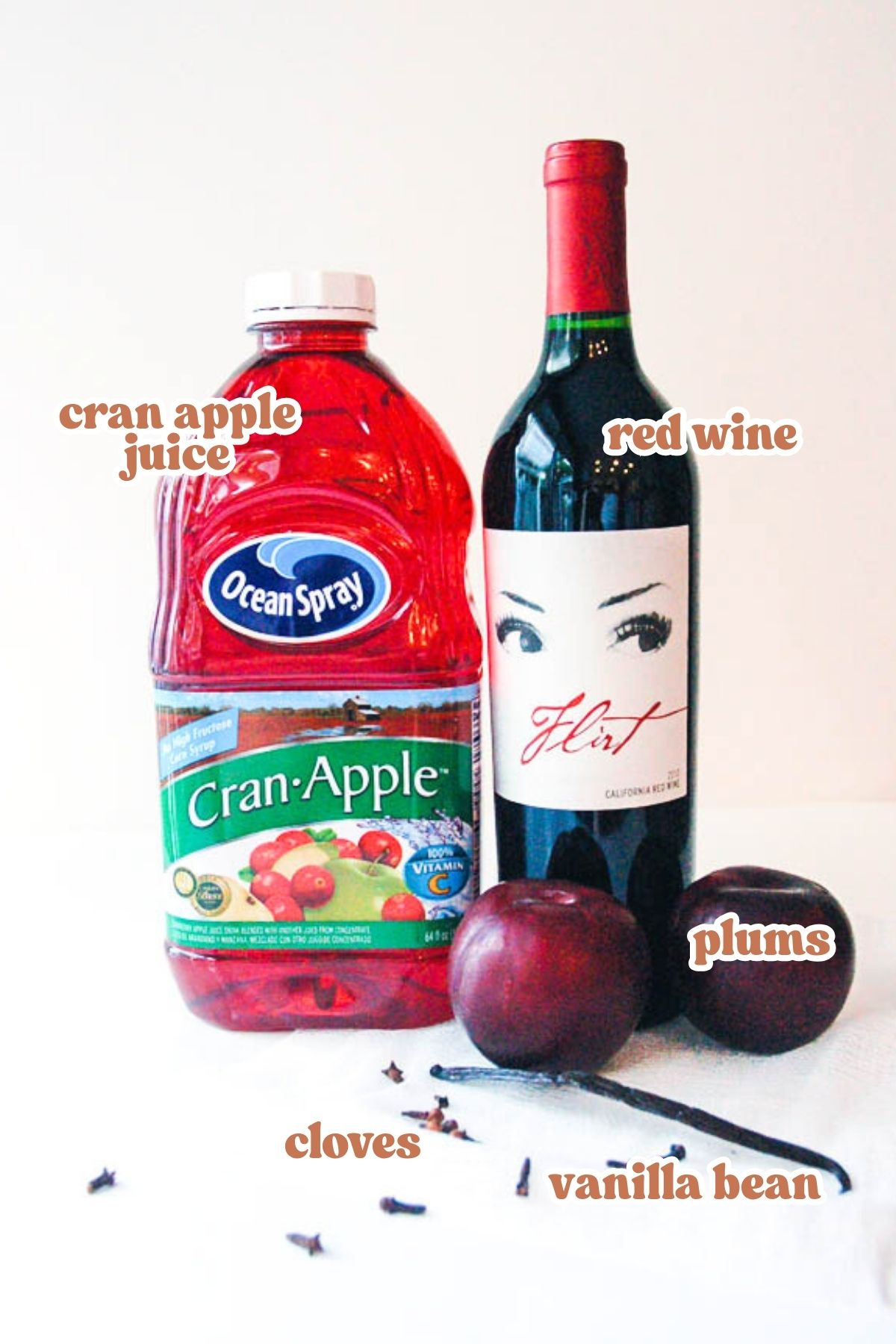 Text: Apple cran juice, red wine, plum, cloves and vanilla bean over an image of the ingredients needed for a sangria.