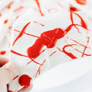A hand holding a piece of Halloween bark made from white chocolate and red icing to look like blood splatters.