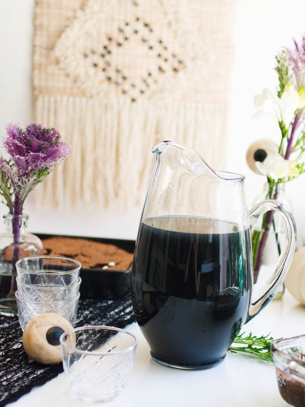 A pitcher holding a black alcoholic punch for Halloween on a party table with spooky decorations.