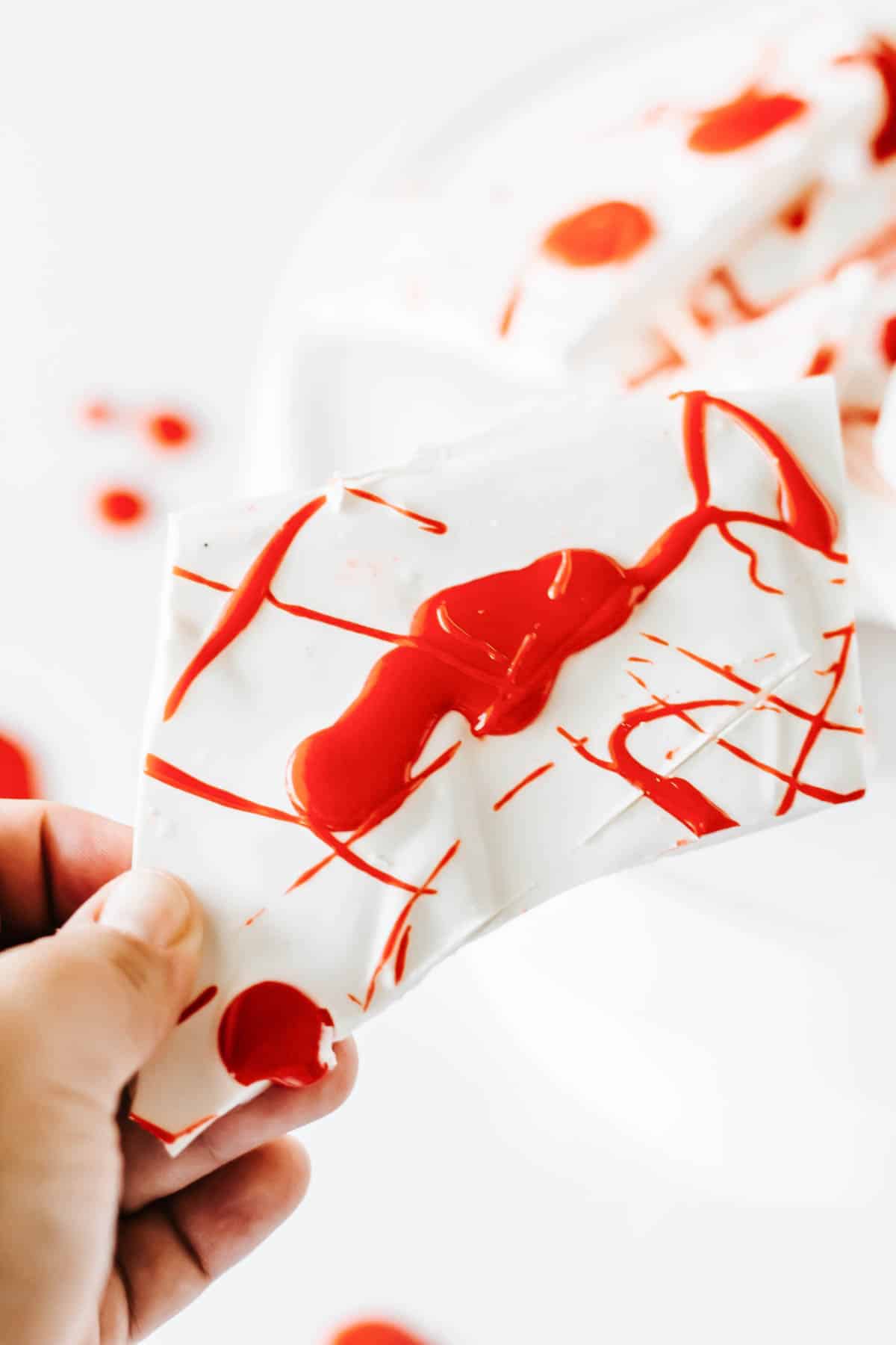 A woman holding a piece of white chocolate bark candy that looks like it's splattered with blood for Halloween.