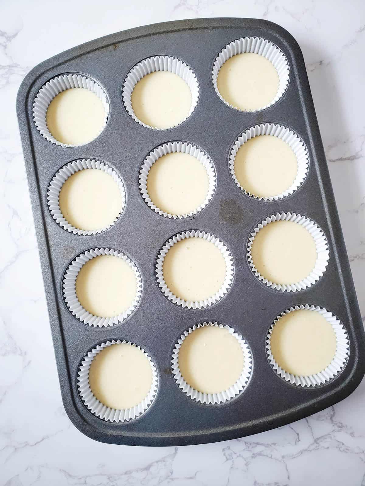 Yellow cake mix cupcake batter portioned on cupcake liners.