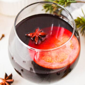 Close up of a glass of mulled wine garnished with a orange wheel and a star anise.
