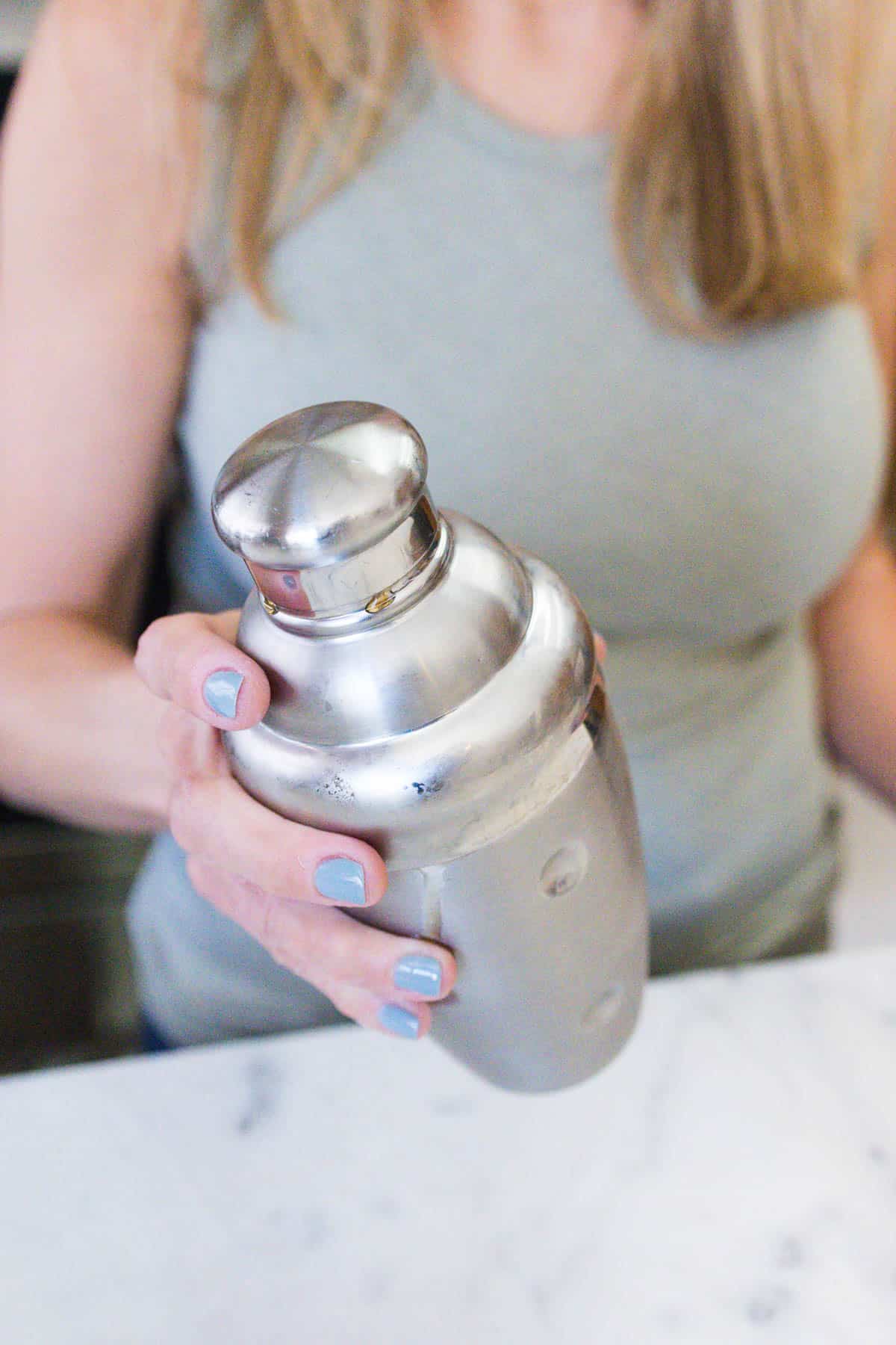 Woman shaking a silver cocktail shaker.