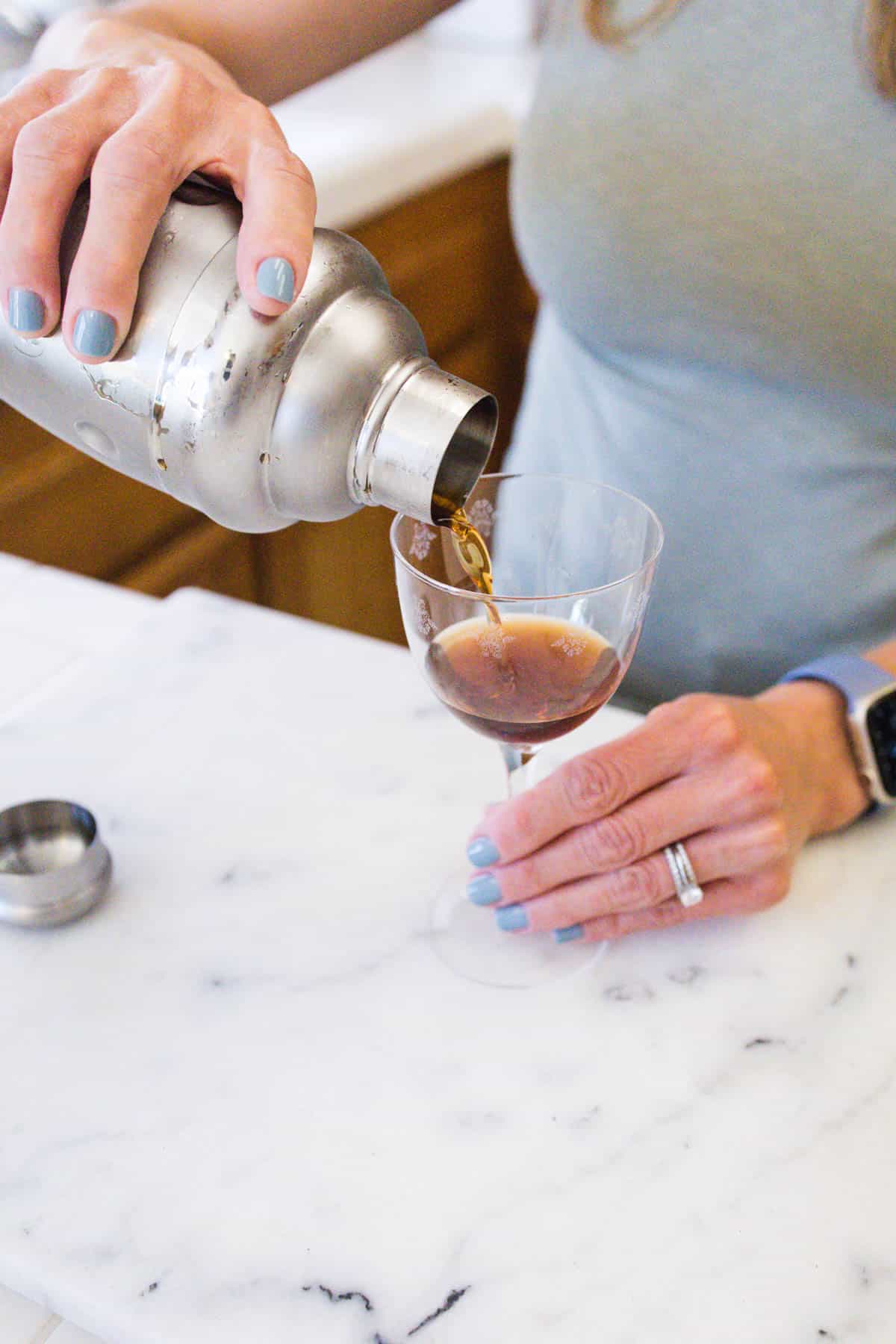 Woman pouring a coffee martini into a glass from a cocktail shaker.