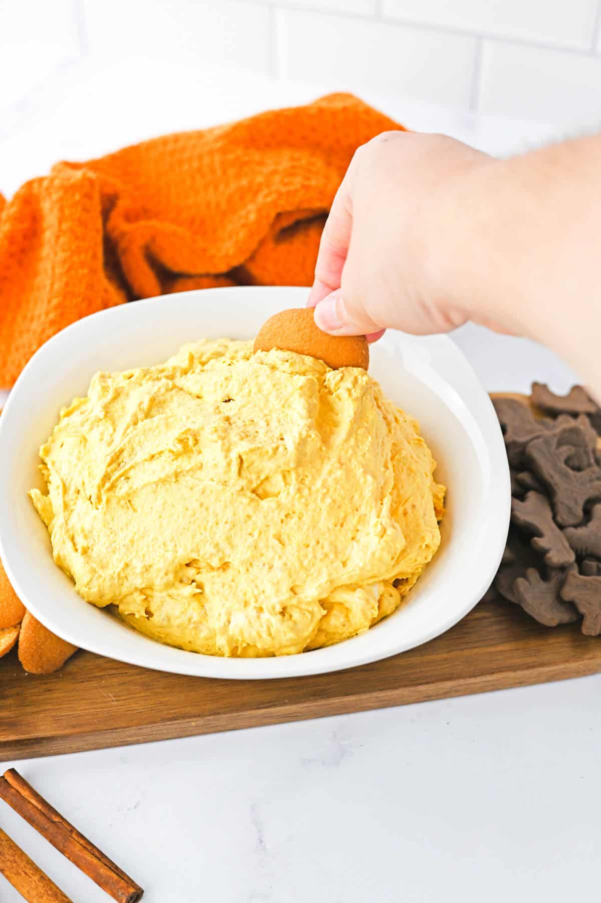 A woman dipping a cookie into a white bowl holding pumpkin dip.