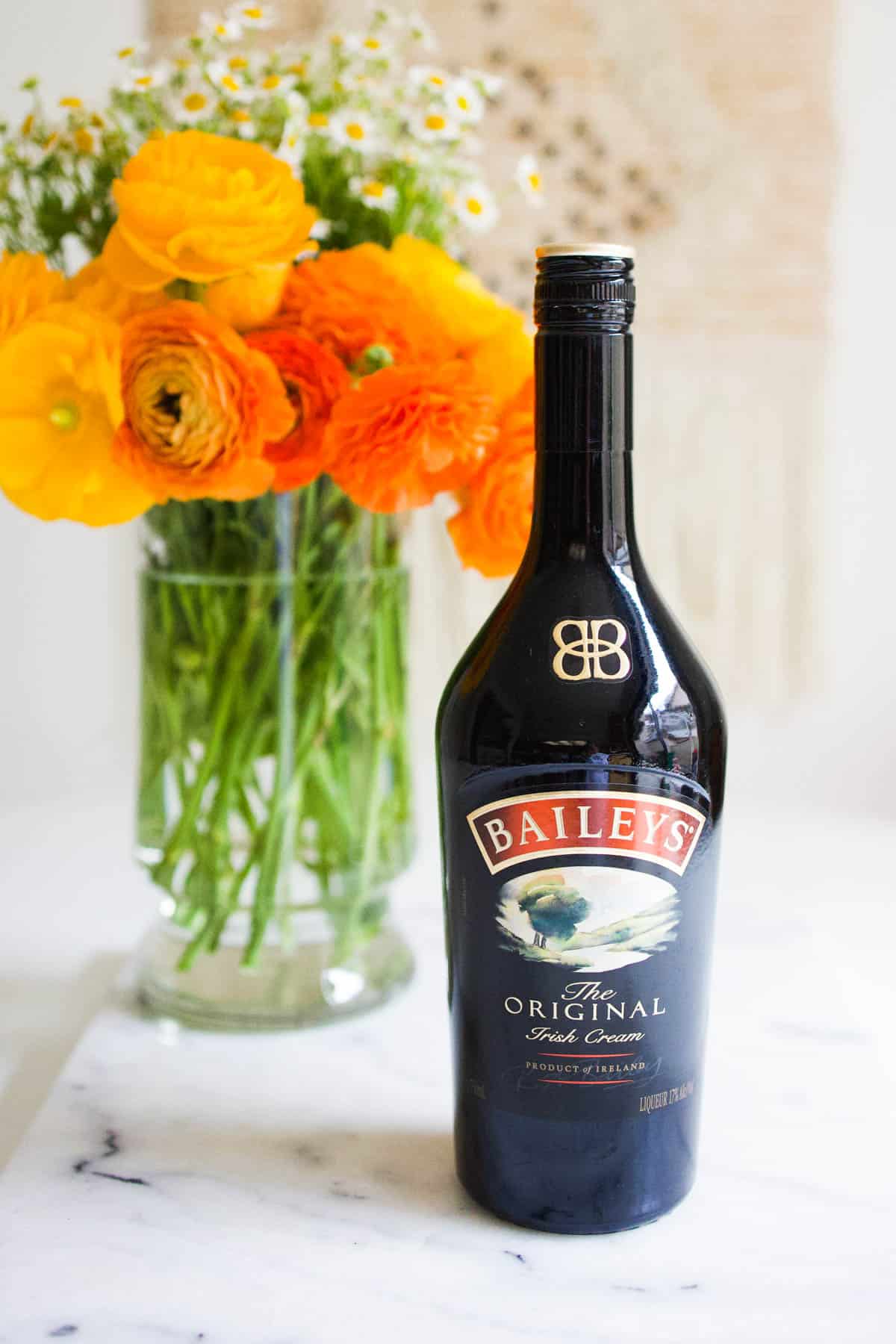 A bottle of Baileys Irish Cream on a table next to a vase of flowers.