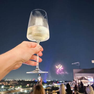A woman's hand holding a glass of wine at a rooftop bar in Anaheim watching the Disneyland fireworks.